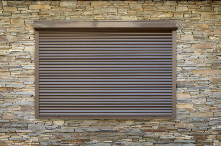 A window with brown metal rolling shutters. Wall decoration with artificial flatten stone